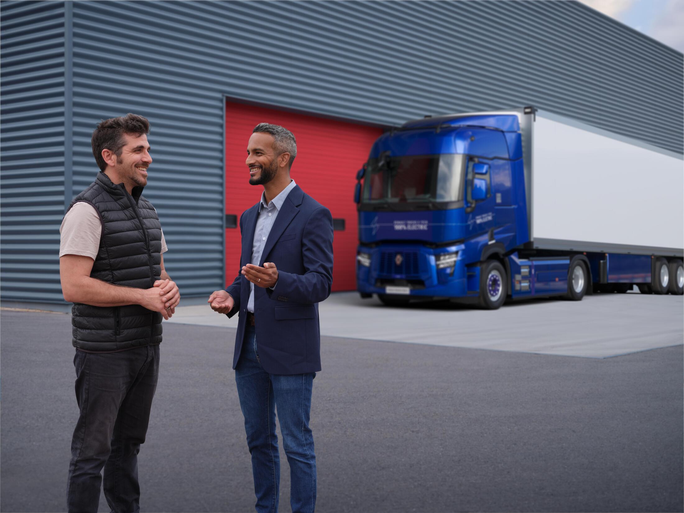 Two men talking in front of a Renault Trucks E-Tech T parked outside a warehouse